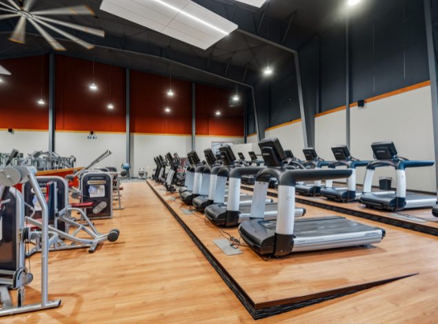 Rows of modern treadmills in the cardio area at Peak Health & Wellness Coeur d'Alene with strength machines in the background.