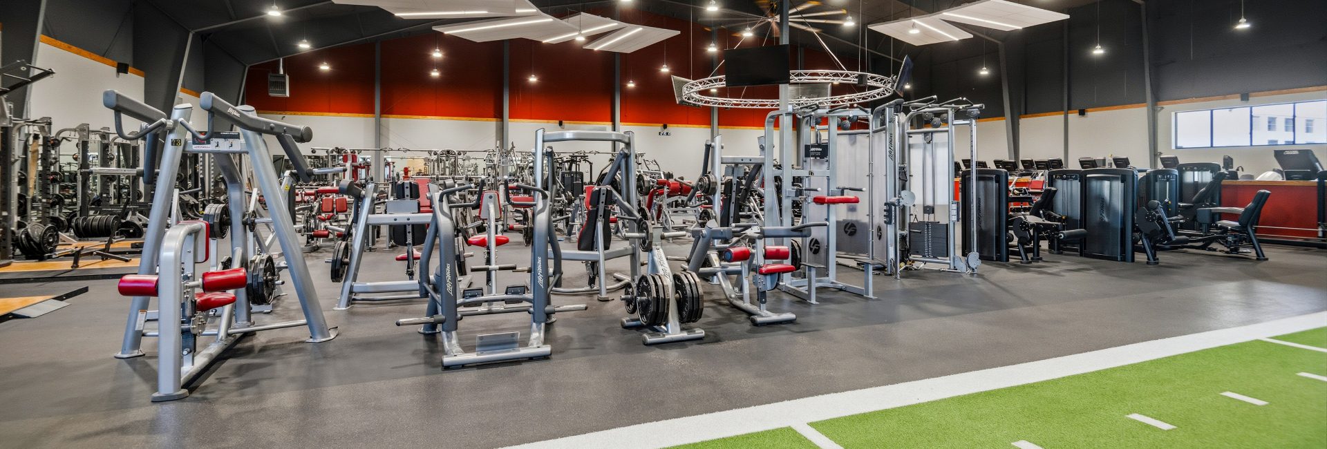Strength training area at Peak Health & Wellness Coeur d'Alene with plate-loaded machines, cable equipment, and turf lane for functional training.