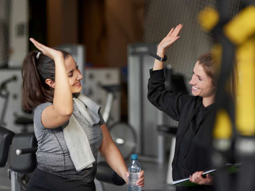 Female personal trainer celebrating client progress with high five at Peak Health & Wellness